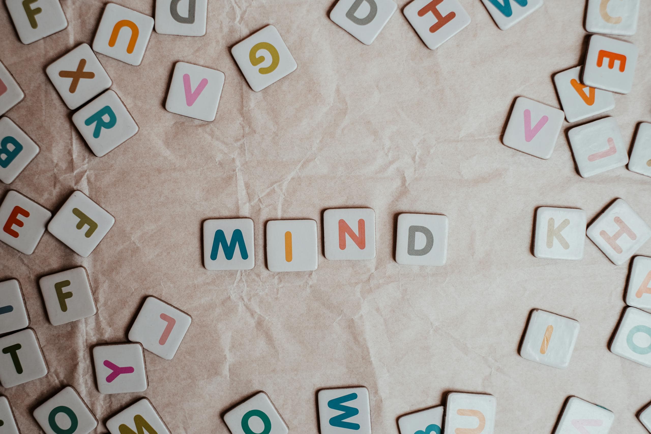 Close-up of scattered letter tiles spelling 'mind' on crumbled paper background to represent subliminals and the subsconsious mind.