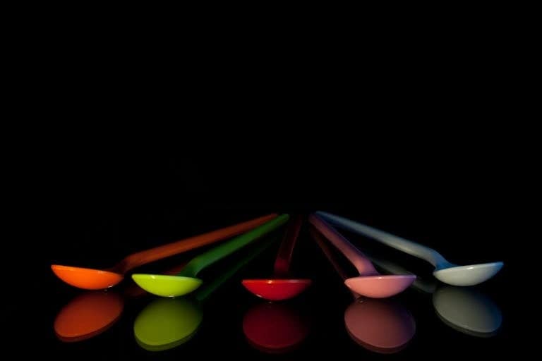 A set of colorful plastic spoons reflected on a black surface with a striking contrast.